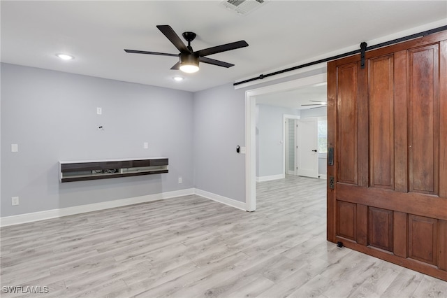 spare room featuring light hardwood / wood-style floors, a barn door, and ceiling fan