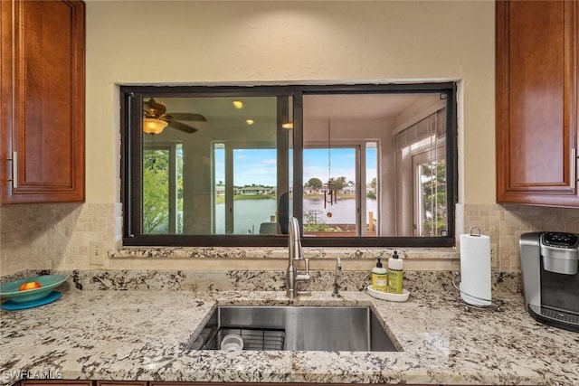 kitchen featuring a water view, sink, backsplash, and light stone counters