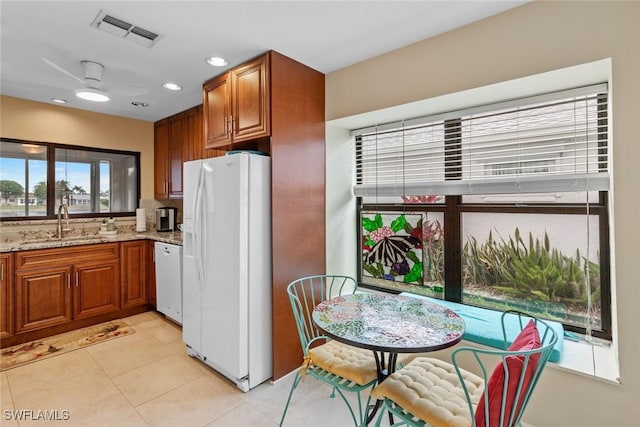 kitchen with sink, white appliances, light tile patterned floors, ceiling fan, and light stone countertops