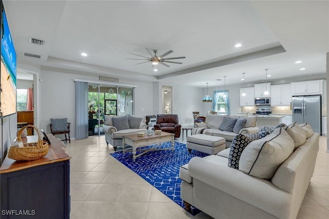 tiled living room featuring ceiling fan and a tray ceiling