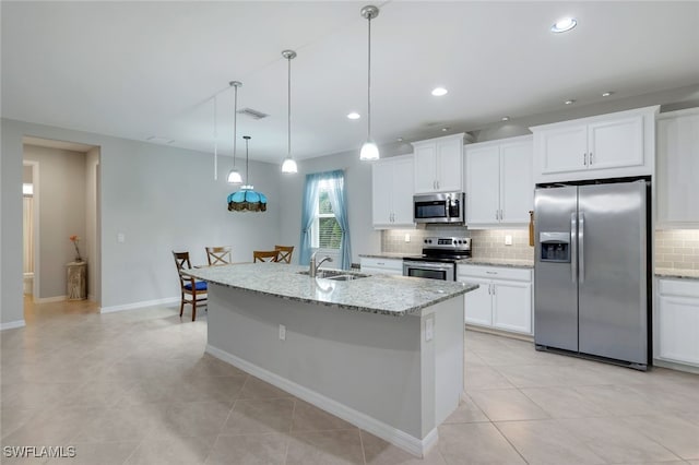 kitchen with white cabinetry, stainless steel appliances, decorative backsplash, light stone counters, and a center island with sink