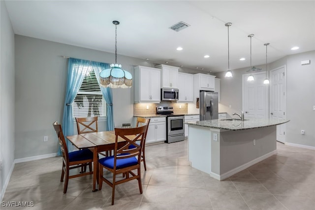 kitchen featuring appliances with stainless steel finishes, white cabinets, pendant lighting, backsplash, and a center island with sink