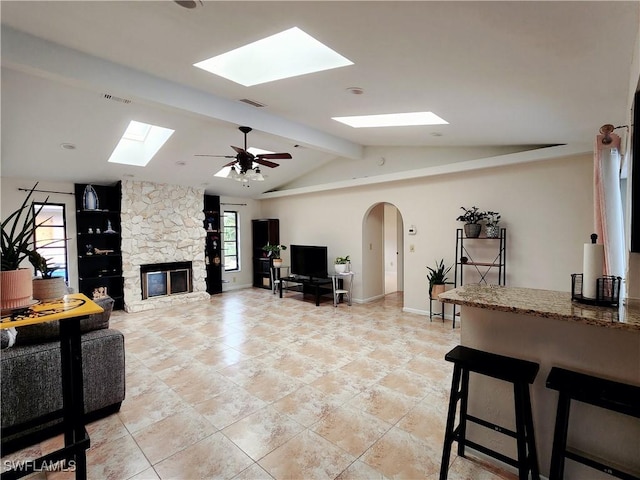 living room featuring vaulted ceiling with beams, a stone fireplace, and ceiling fan