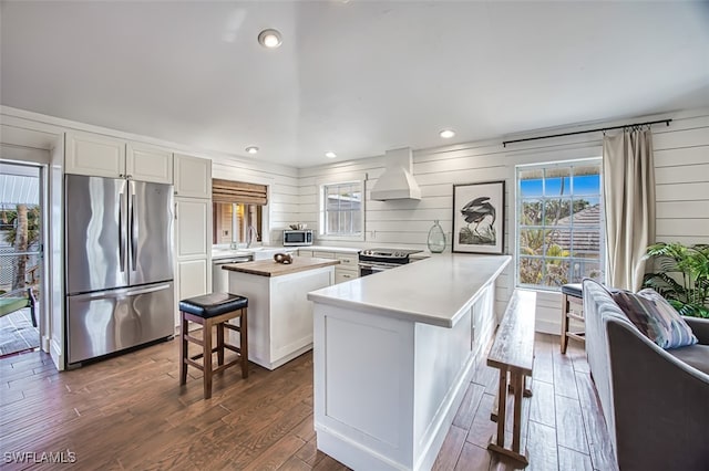 kitchen featuring dark hardwood / wood-style floors, premium range hood, a center island, a kitchen bar, and stainless steel appliances