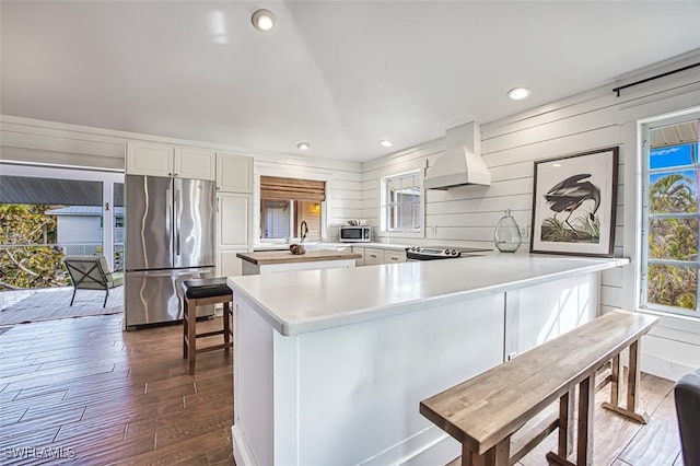 kitchen with dark hardwood / wood-style floors, wood walls, custom exhaust hood, white cabinetry, and stainless steel appliances