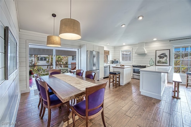 dining area featuring light wood-type flooring, plenty of natural light, and wood walls