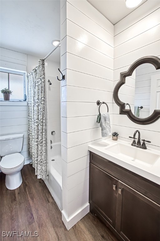 full bathroom featuring toilet, hardwood / wood-style floors, wooden walls, shower / bathtub combination with curtain, and vanity