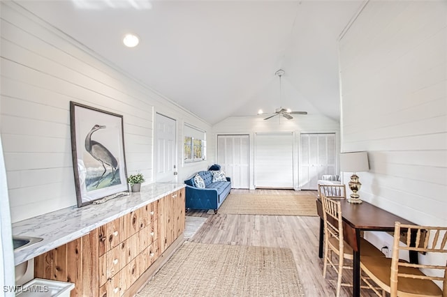 hall with lofted ceiling, light hardwood / wood-style flooring, and wooden walls