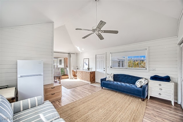 living room with ceiling fan, wood walls, and light wood-type flooring