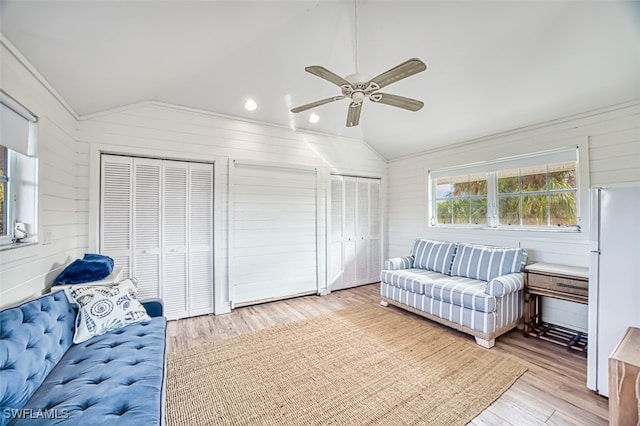 living room with ceiling fan, vaulted ceiling, wood walls, and light hardwood / wood-style flooring