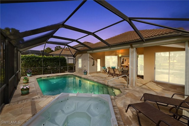 pool at dusk featuring an in ground hot tub, a patio, and glass enclosure