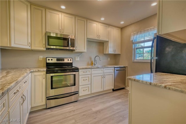 kitchen featuring stainless steel appliances, light hardwood / wood-style floors, sink, and light stone countertops