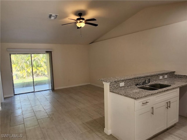 kitchen featuring lofted ceiling, ceiling fan, sink, white cabinetry, and light stone counters