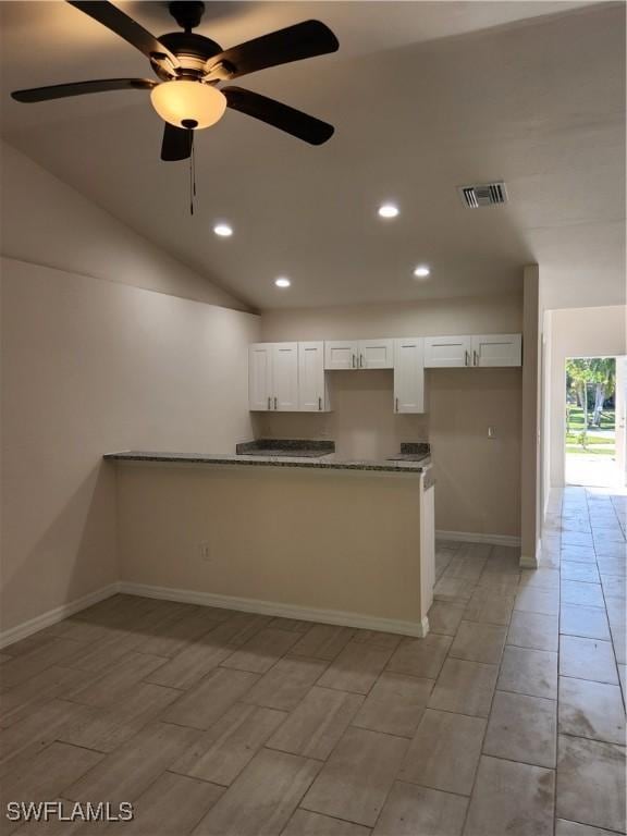 kitchen with white cabinetry, kitchen peninsula, ceiling fan, vaulted ceiling, and stone counters