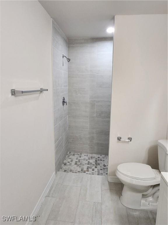 bathroom with toilet, a tile shower, and vanity