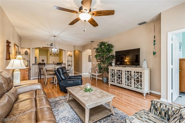 living room featuring ceiling fan with notable chandelier and light hardwood / wood-style flooring