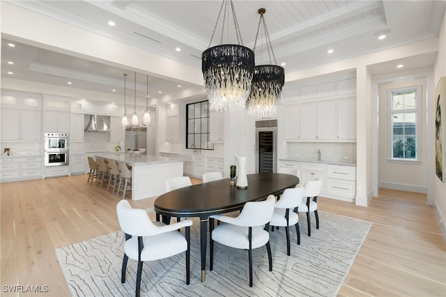 dining room with wine cooler, a raised ceiling, a chandelier, and light hardwood / wood-style flooring