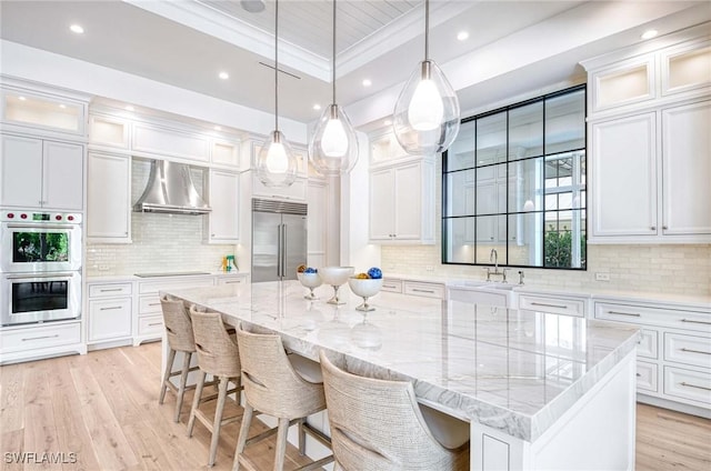 460 2nd Ave N, Naples, FL 34102 - kitchen with stainless steel appliances, wall chimney range hood, light wood-style floors, white cabinets, and recessed lighting