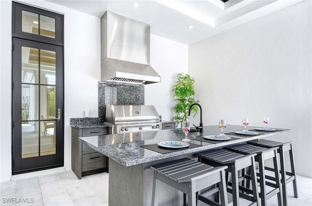 460 2nd Ave N, Naples, FL 34102 - kitchen with wall chimney exhaust hood, a breakfast bar, dark stone counters, a sink, and recessed lighting