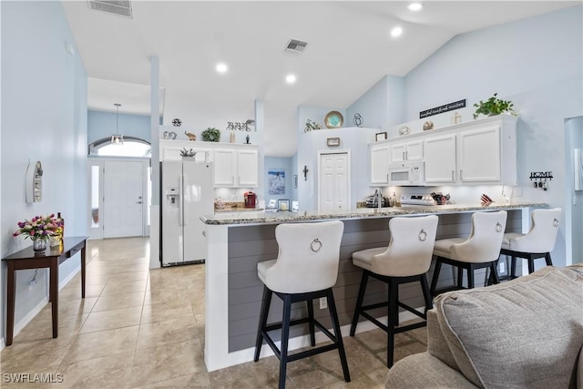 kitchen featuring a kitchen bar, light stone counters, white cabinets, and white appliances