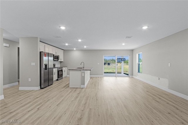 kitchen with appliances with stainless steel finishes, white cabinetry, sink, a kitchen island with sink, and light wood-type flooring