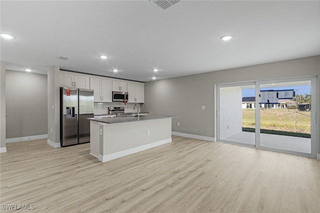 kitchen featuring appliances with stainless steel finishes, dark stone countertops, light hardwood / wood-style flooring, and white cabinetry