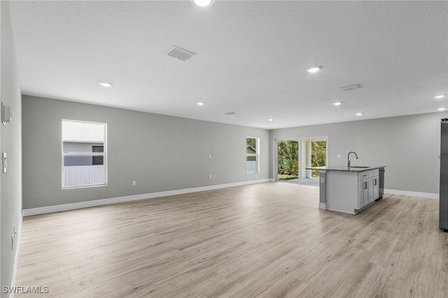 337 Woodburn Dr, Lehigh Acres, FL 33972 - unfurnished living room featuring a sink, light wood-type flooring, baseboards, recessed lighting, and a textured ceiling