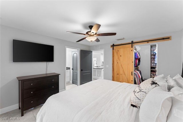 bedroom featuring ceiling fan, a barn door, a spacious closet, connected bathroom, and a closet