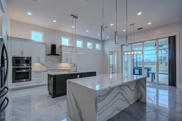 kitchen featuring hanging light fixtures, black appliances, wall chimney exhaust hood, and a center island with sink