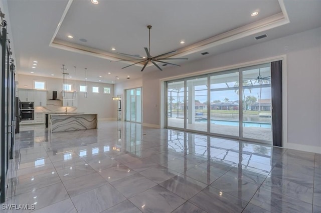 unfurnished living room featuring ceiling fan and a tray ceiling