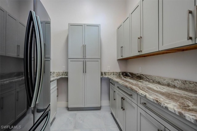 kitchen with black refrigerator, gray cabinets, and light stone countertops