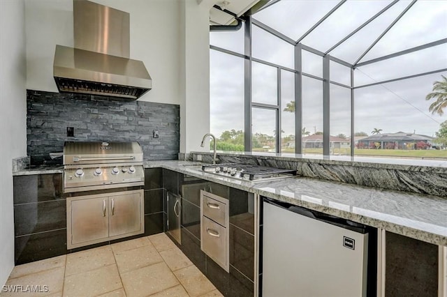 kitchen with wall chimney exhaust hood, sink, tasteful backsplash, stainless steel fridge, and light stone countertops