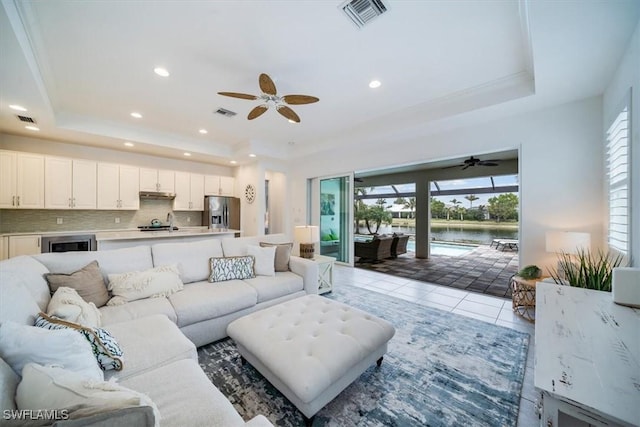 living room featuring ceiling fan, tile patterned flooring, a water view, and a raised ceiling