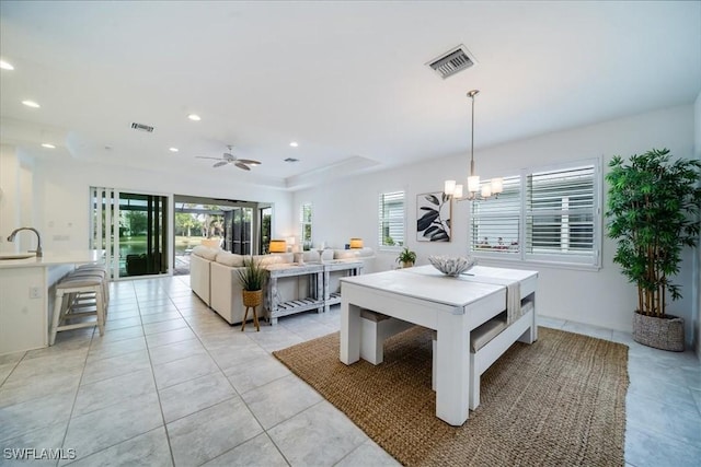 dining space with light tile patterned floors, ceiling fan with notable chandelier, a raised ceiling, and sink