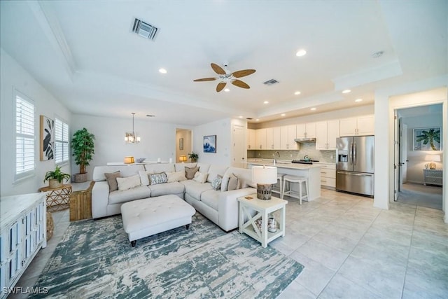 living room with ceiling fan with notable chandelier, sink, and a tray ceiling