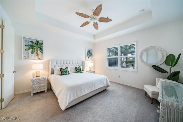 bedroom with ceiling fan, light colored carpet, and a tray ceiling