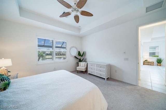 carpeted bedroom with ceiling fan and a tray ceiling