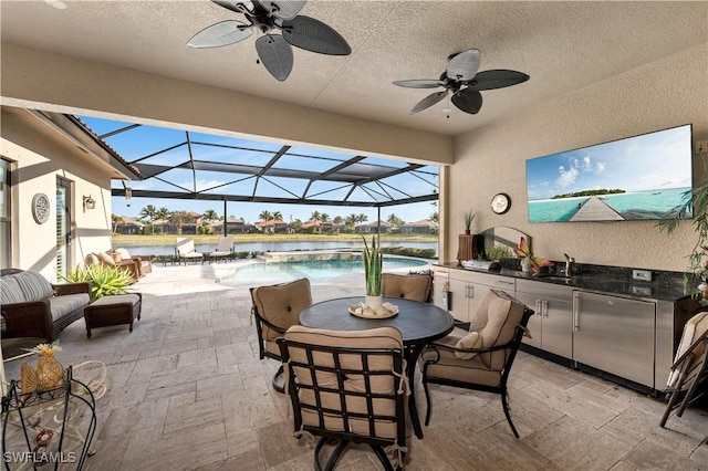 view of patio / terrace with ceiling fan, sink, glass enclosure, and an outdoor kitchen