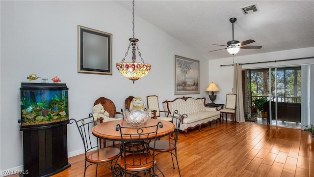 dining area with wood-type flooring, a textured ceiling, and vaulted ceiling