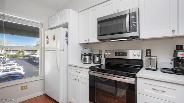 kitchen with light wood-type flooring, appliances with stainless steel finishes, white cabinets, and light stone counters