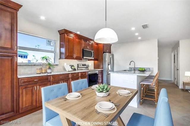 kitchen with decorative backsplash, a kitchen bar, sink, hanging light fixtures, and stainless steel appliances