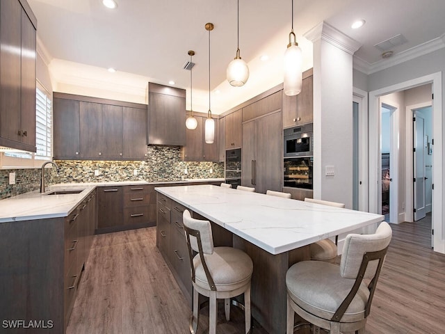 kitchen featuring wood-type flooring, hanging light fixtures, sink, a center island, and wall chimney range hood