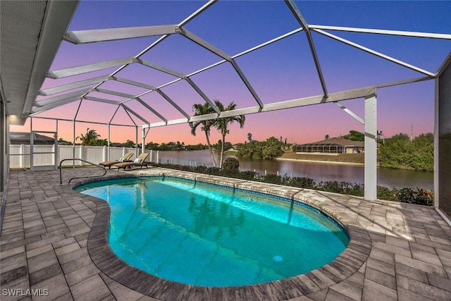 pool at dusk featuring glass enclosure, a water view, and a patio