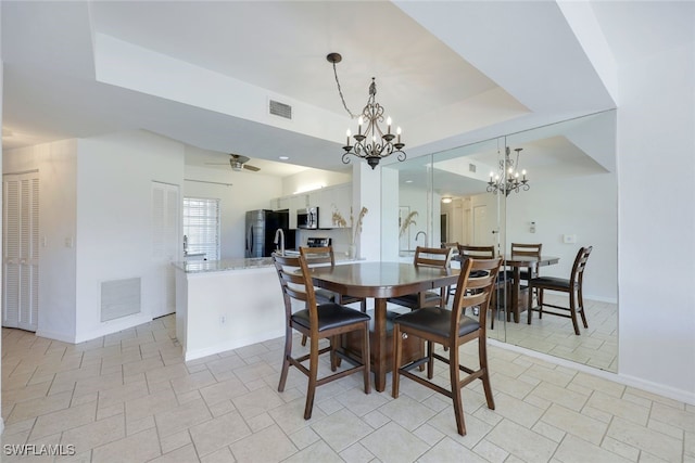 dining room with ceiling fan with notable chandelier and a tray ceiling