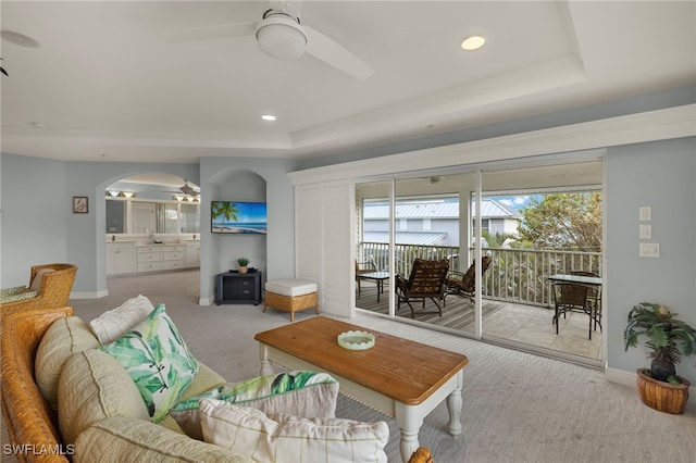 living room with ceiling fan, a wealth of natural light, a raised ceiling, and light colored carpet