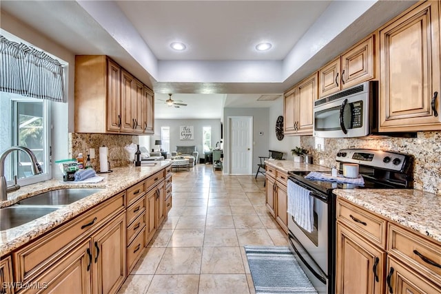 kitchen with ceiling fan, appliances with stainless steel finishes, sink, light stone countertops, and decorative backsplash