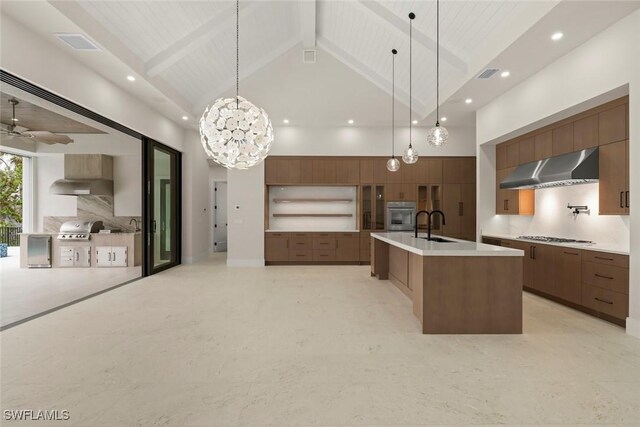 kitchen featuring stainless steel appliances, decorative light fixtures, a center island with sink, and wall chimney exhaust hood