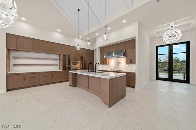 kitchen with a large island with sink, wall chimney exhaust hood, hanging light fixtures, oven, and gas stovetop