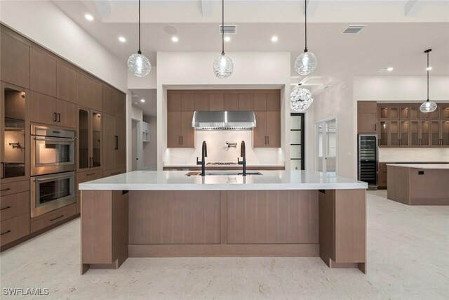 kitchen featuring pendant lighting, a breakfast bar, a large island with sink, range hood, and stainless steel double oven