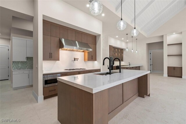 kitchen with a spacious island, hanging light fixtures, sink, wall chimney exhaust hood, and lofted ceiling with beams